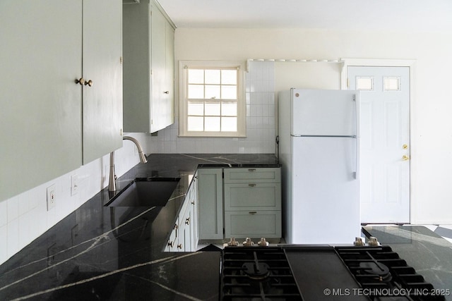 kitchen with tasteful backsplash, freestanding refrigerator, dark countertops, cooktop, and a sink