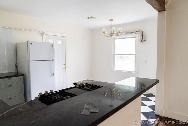 kitchen featuring an inviting chandelier, freestanding refrigerator, dark countertops, visible vents, and dark floors