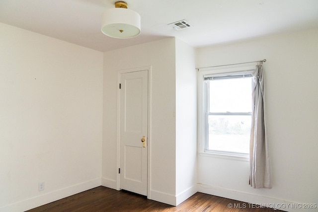 empty room featuring visible vents, baseboards, and dark wood finished floors