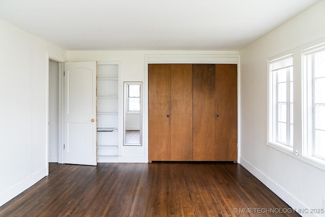 unfurnished bedroom with a closet, dark wood-style flooring, and baseboards