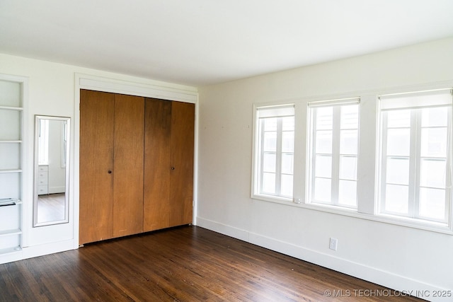 unfurnished bedroom featuring dark wood-type flooring, a closet, and baseboards