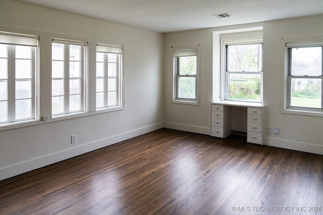 unfurnished room with dark wood finished floors, visible vents, baseboards, and a healthy amount of sunlight