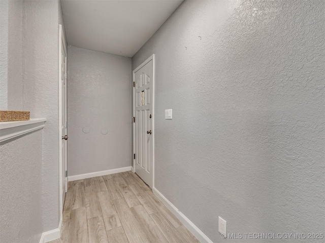 hall featuring a textured wall, light wood-type flooring, and baseboards