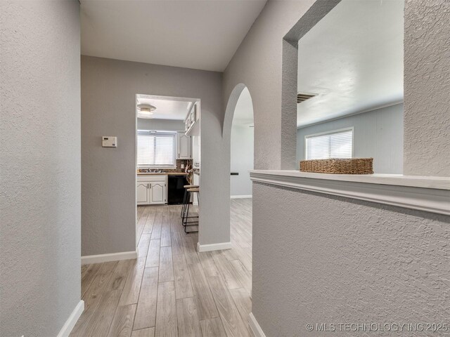 corridor featuring a textured wall, plenty of natural light, light wood-style flooring, and arched walkways