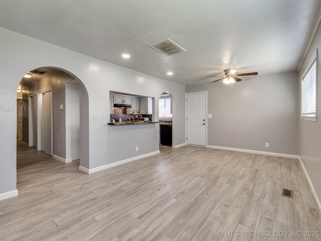 unfurnished living room with visible vents, arched walkways, plenty of natural light, ceiling fan, and light wood-style floors