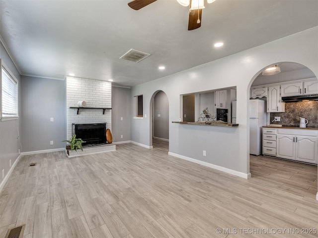 unfurnished living room with arched walkways, a brick fireplace, visible vents, and ceiling fan