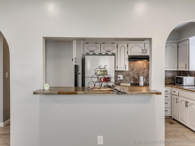 kitchen featuring white appliances, arched walkways, light wood-type flooring, under cabinet range hood, and backsplash