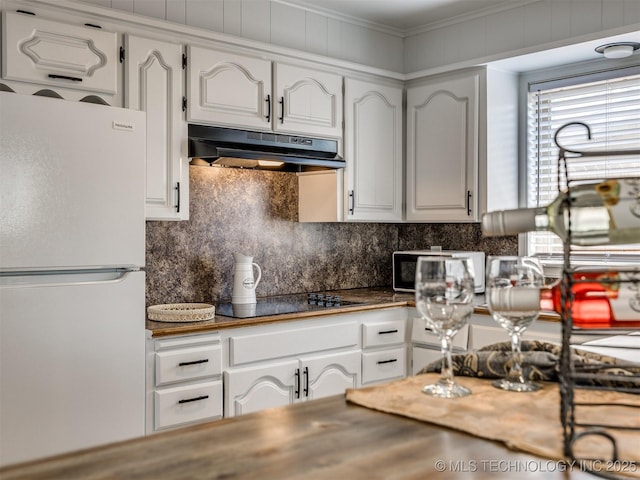 kitchen featuring under cabinet range hood, freestanding refrigerator, dark countertops, and white cabinets