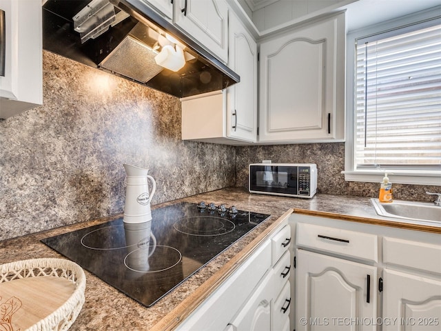kitchen with under cabinet range hood, tasteful backsplash, white cabinetry, and black electric stovetop