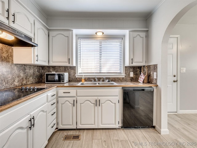 kitchen featuring tasteful backsplash, black appliances, under cabinet range hood, a sink, and light wood finished floors