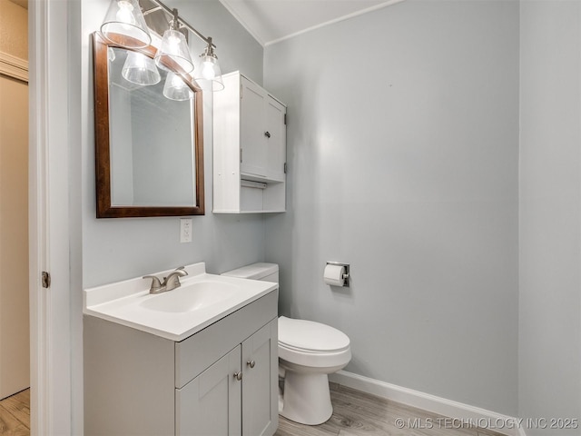 half bath with vanity, baseboards, ornamental molding, toilet, and wood finished floors