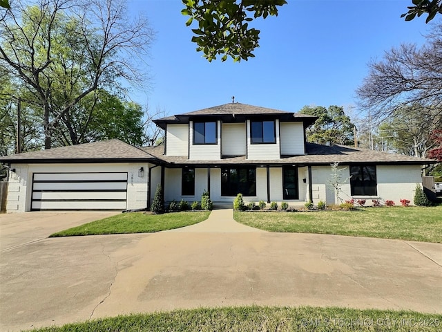 prairie-style home with an attached garage, roof with shingles, concrete driveway, and a front lawn