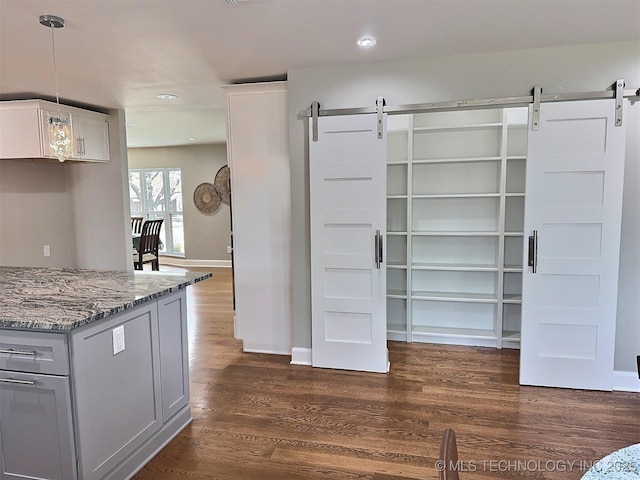 kitchen with light stone counters, baseboards, dark wood-style floors, and a barn door