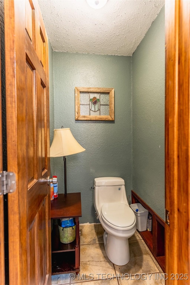 bathroom with toilet, a textured ceiling, and a textured wall