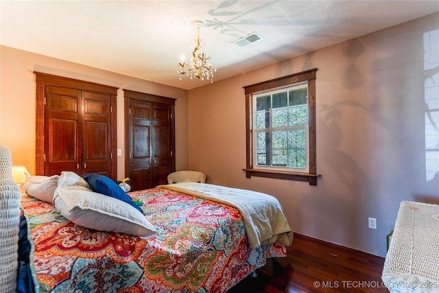 bedroom with an inviting chandelier, visible vents, wood finished floors, multiple closets, and baseboards