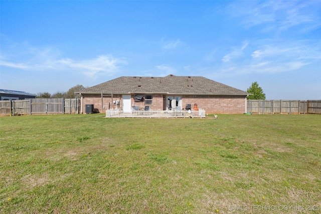 rear view of house with brick siding, a fenced backyard, and a lawn