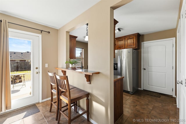 kitchen with stainless steel fridge with ice dispenser, baseboards, a peninsula, brown cabinets, and a breakfast bar area