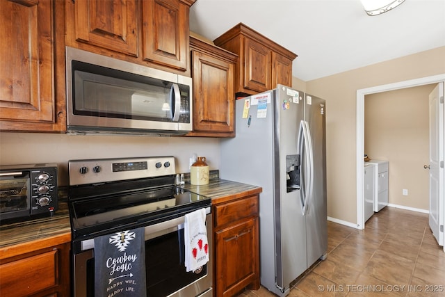 kitchen with baseboards, washer and dryer, dark countertops, appliances with stainless steel finishes, and brown cabinetry
