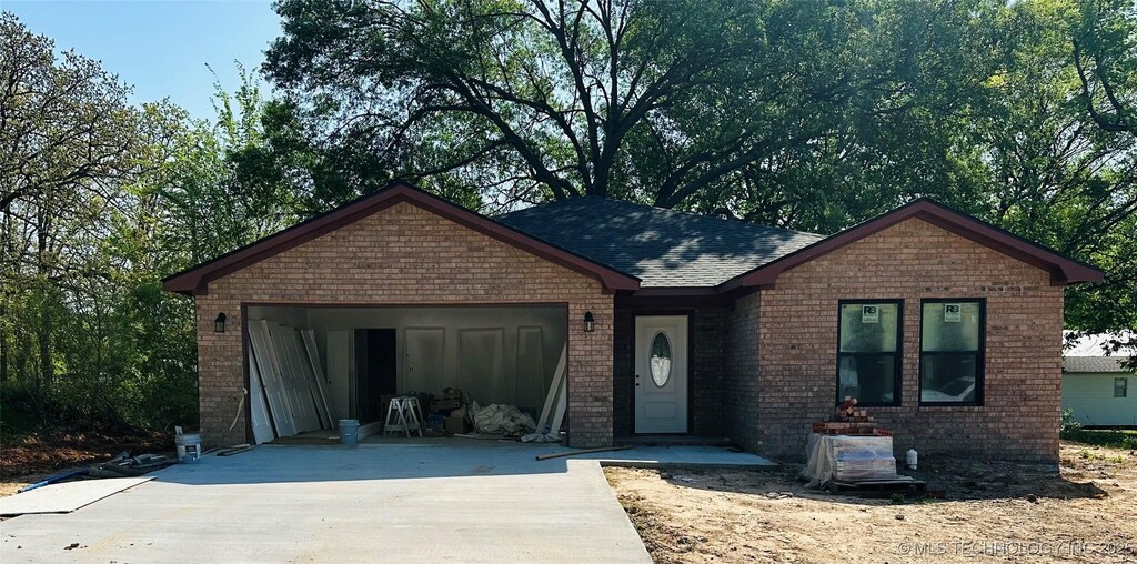ranch-style house featuring an attached garage, a shingled roof, concrete driveway, and brick siding