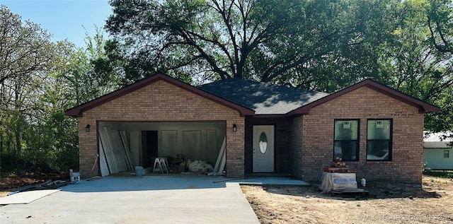 ranch-style house featuring an attached garage, a shingled roof, concrete driveway, and brick siding