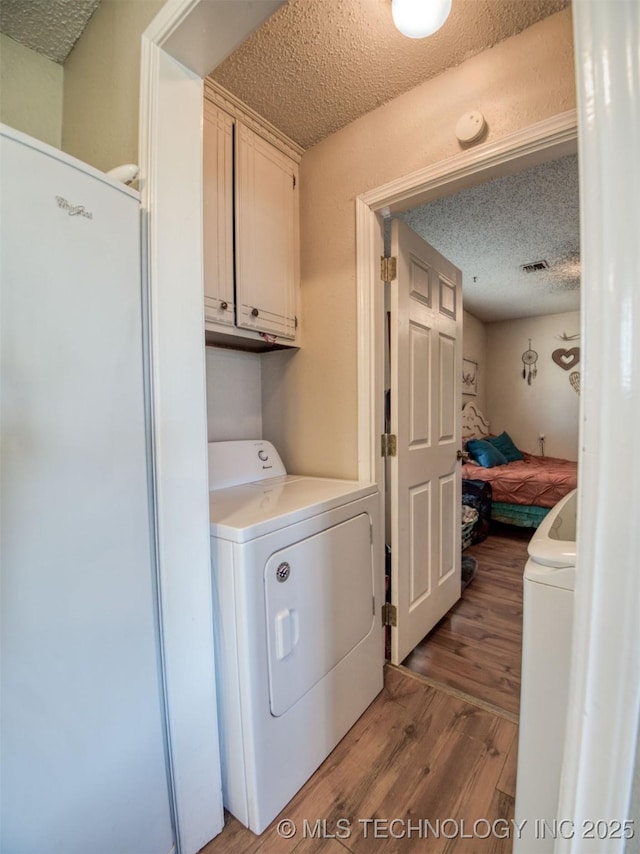 22526 N 2860th Rd, Kingfisher, OK 73750 - laundry room with washer and dryer, a textured ceiling, wood finished floors, and cabinet space
