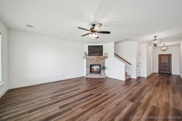 unfurnished living room featuring a brick fireplace, dark wood finished floors, visible vents, and stairway