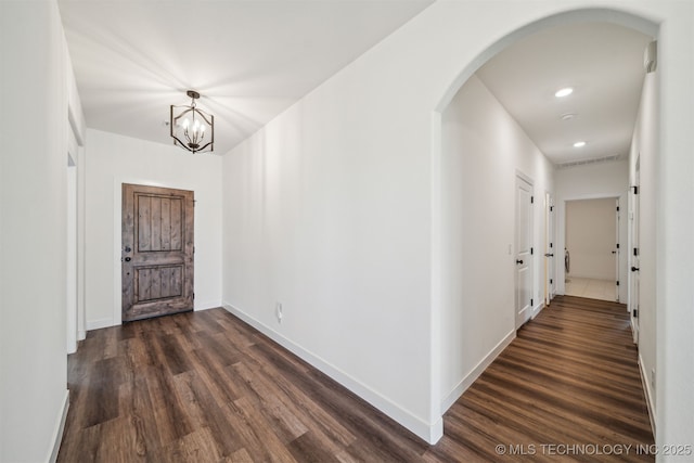 hallway with visible vents, baseboards, arched walkways, a notable chandelier, and dark wood-style flooring