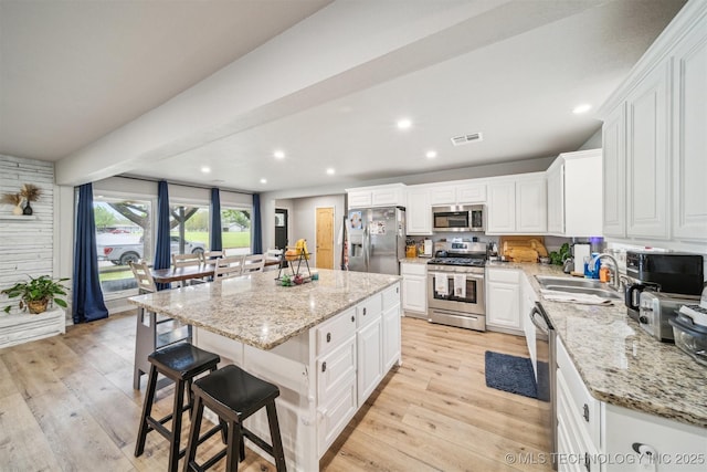 kitchen featuring light wood finished floors, a sink, a kitchen island, appliances with stainless steel finishes, and white cabinetry