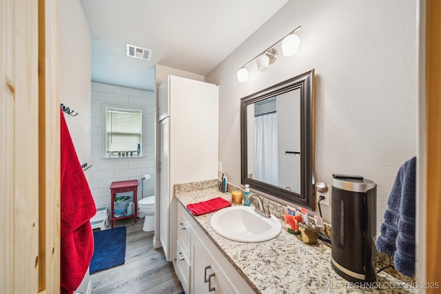 full bath featuring wood finished floors, visible vents, toilet, vanity, and tile walls