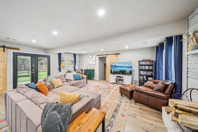 living area featuring a barn door, light wood finished floors, visible vents, and recessed lighting