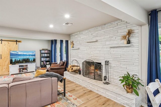 living room featuring a barn door, recessed lighting, wood finished floors, visible vents, and a stone fireplace