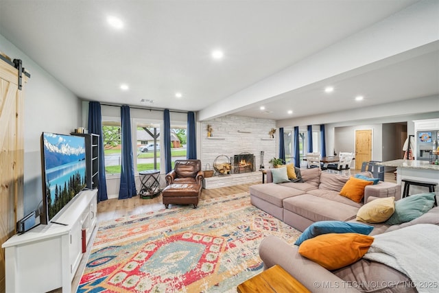 living area with a barn door, wood finished floors, beamed ceiling, a fireplace, and recessed lighting