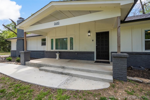 doorway to property with board and batten siding, a chimney, and brick siding