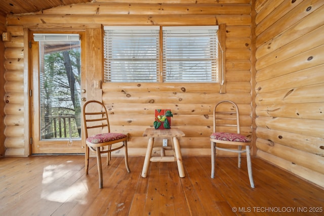 sitting room featuring log walls, vaulted ceiling, and hardwood / wood-style flooring