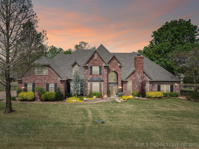 french provincial home featuring brick siding, a front yard, a chimney, and roof with shingles