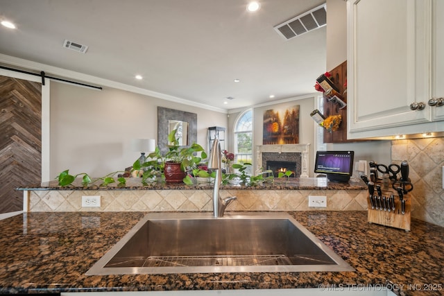 kitchen featuring visible vents, a lit fireplace, a sink, and decorative backsplash