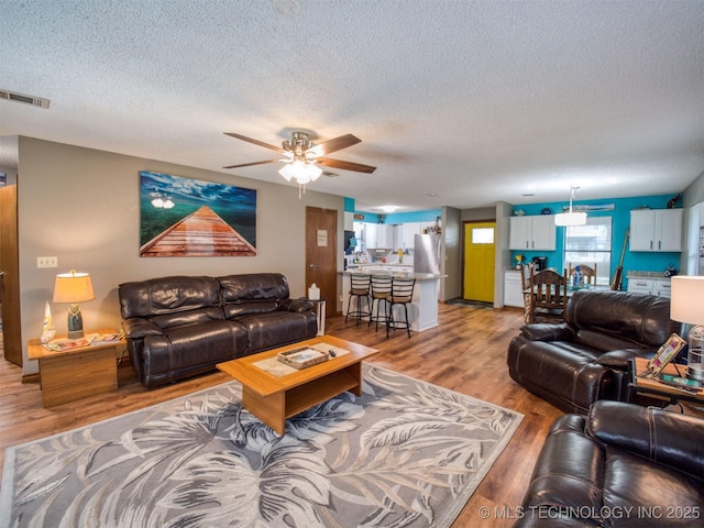1668 Waters Rd, Kingston, OK 73439 - living room with a textured ceiling, light wood finished floors, a ceiling fan, and visible vents