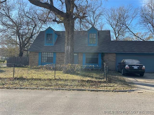 1204 N Detroit Ave, Tulsa, OK 74106 - new england style home featuring a garage, concrete driveway, a fenced front yard, brick siding, and roof with shingles
