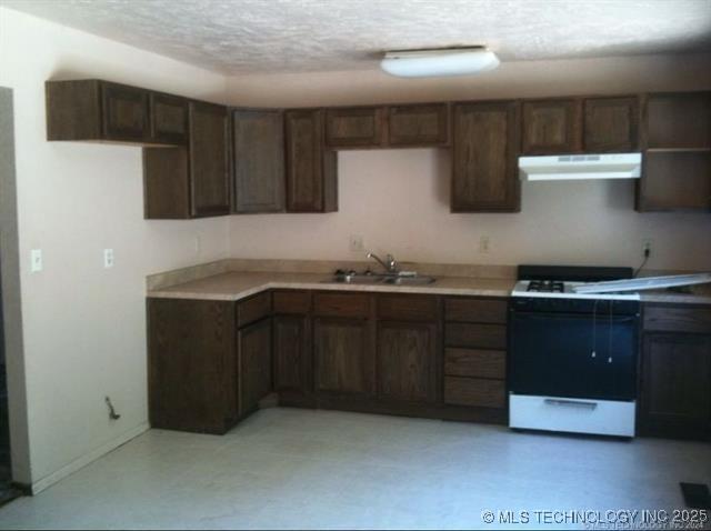 1204 N Detroit Ave, Tulsa, OK 74106 - kitchen featuring a textured ceiling, gas range gas stove, under cabinet range hood, light countertops, and a sink