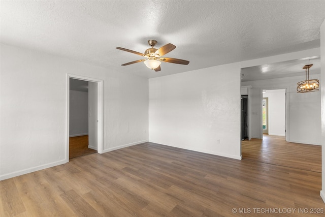 empty room with a textured ceiling, ceiling fan with notable chandelier, wood finished floors, and baseboards
