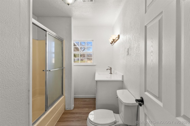 full bath featuring bath / shower combo with glass door, toilet, a textured wall, vanity, and wood finished floors