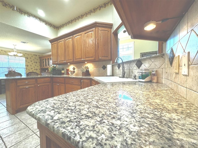 kitchen with visible vents, a notable chandelier, a sink, a peninsula, and decorative backsplash