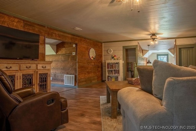 living room featuring wood finished floors, wooden walls, a ceiling fan, and visible vents