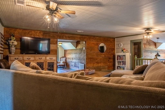 living room featuring wooden walls, visible vents, ceiling fan, and ornamental molding