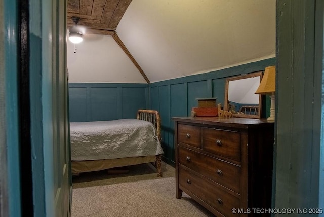 bedroom with a decorative wall, wainscoting, carpet, and vaulted ceiling