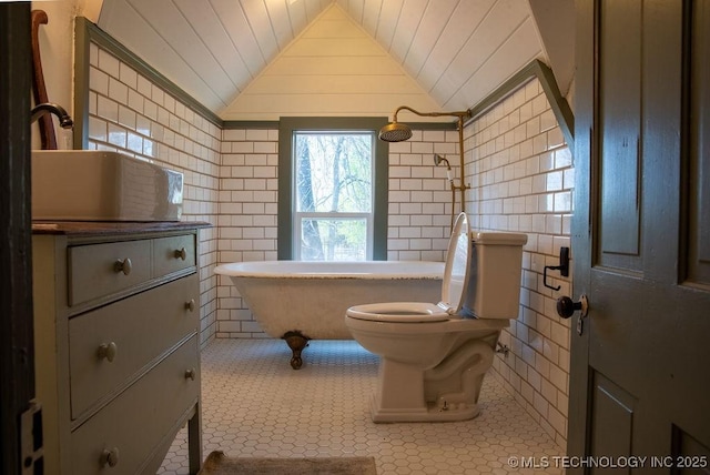 bathroom with a freestanding tub, tile patterned floors, toilet, lofted ceiling, and tile walls