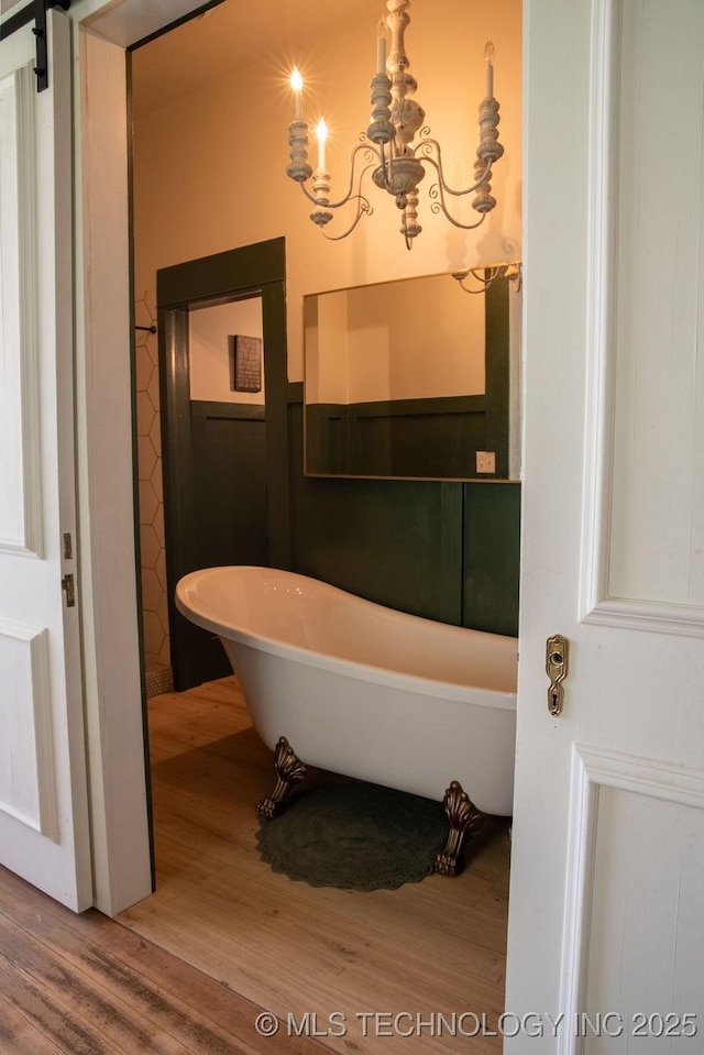 bathroom with a chandelier, a freestanding bath, and wood finished floors