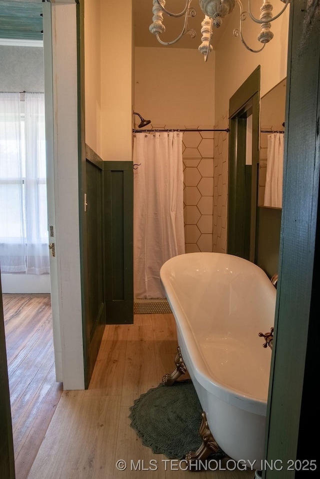 full bathroom with a wainscoted wall, an inviting chandelier, a soaking tub, and wood finished floors