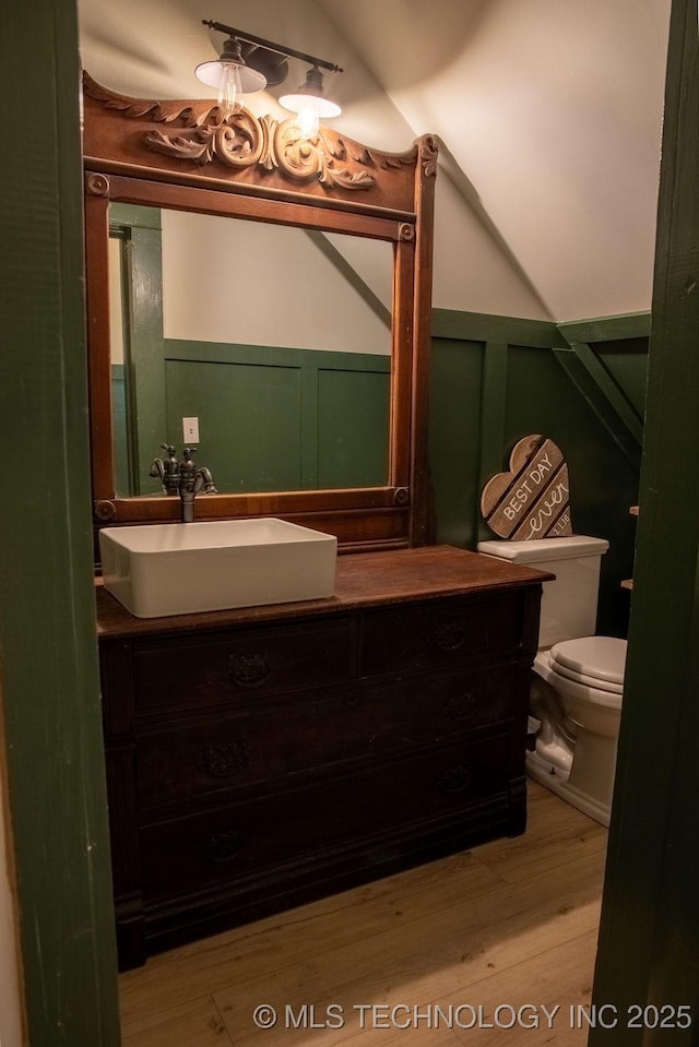bathroom featuring a decorative wall, toilet, vanity, wood finished floors, and a wainscoted wall