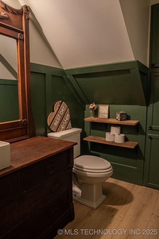 half bath featuring toilet, vanity, wood finished floors, and lofted ceiling